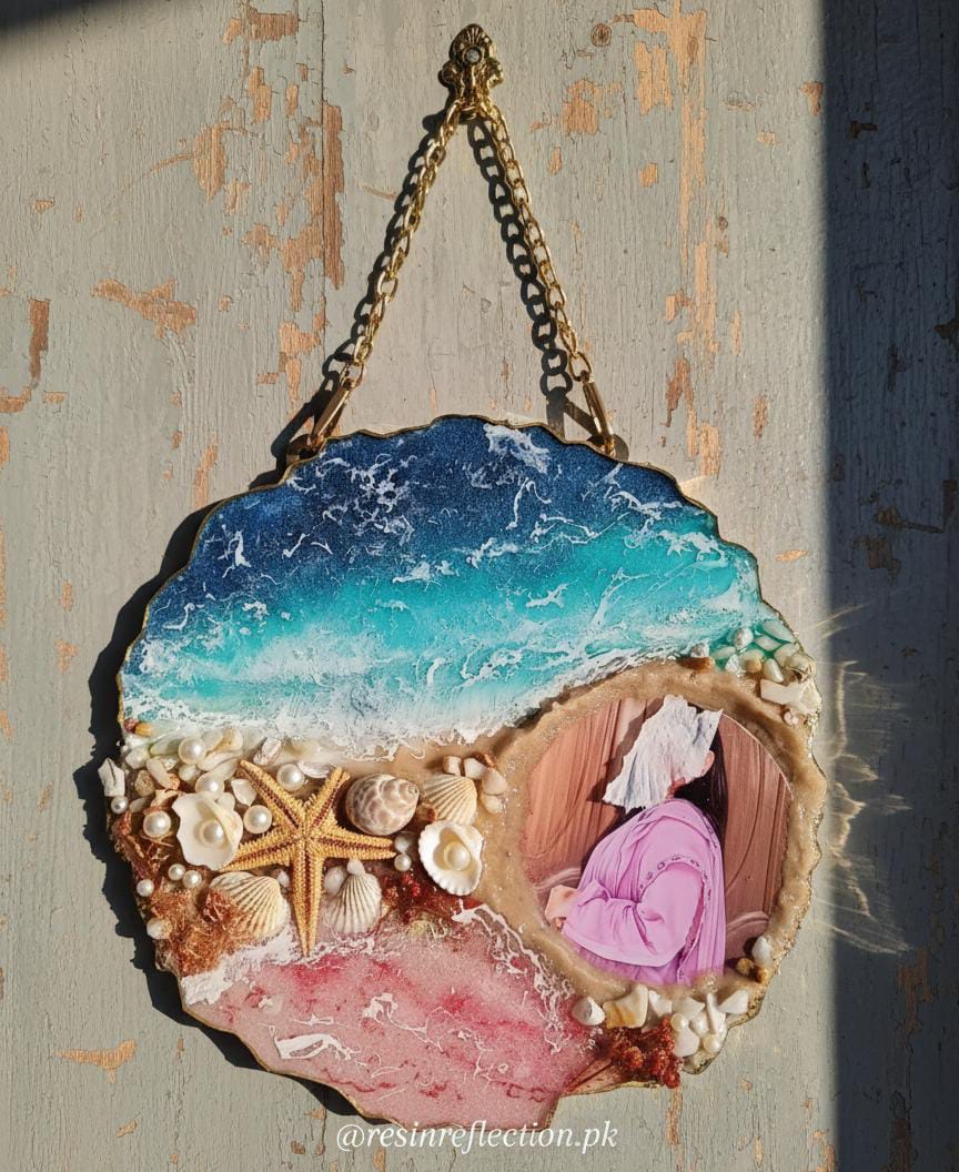 Decorative piece with ocean scene and person in pink dress, mounted on a textured wall.