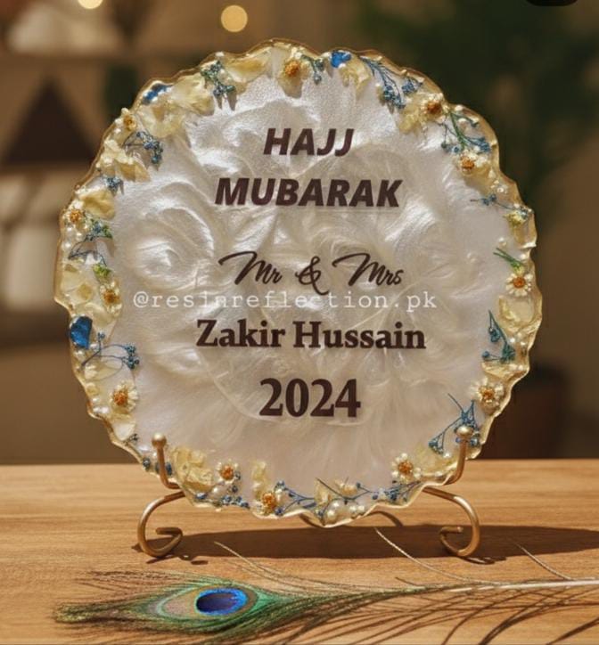 Decorative plate with 'Hajj Mubarak' text and floral design on a stand.