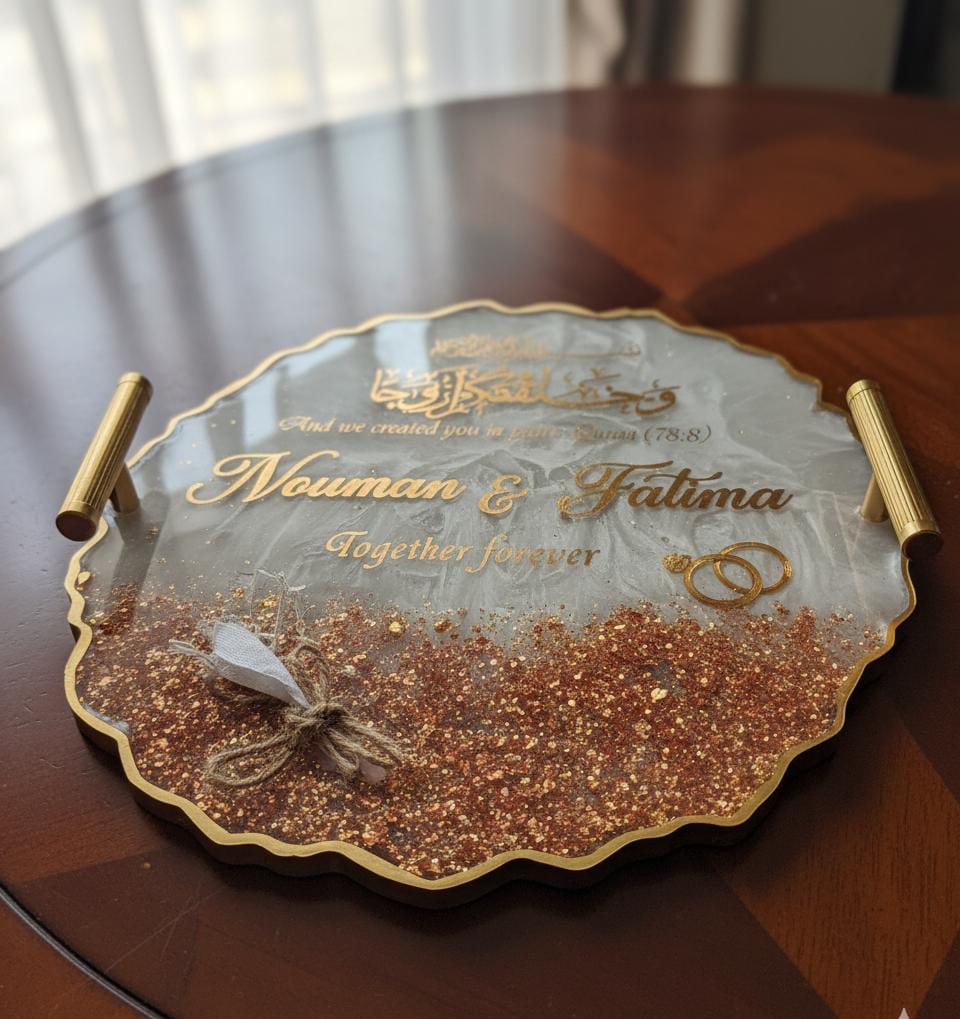 Decorative glass tray with gold handles and engraved text on a wooden surface