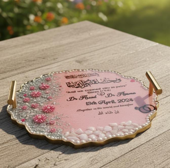 Decorative tray with floral patterns and text on a wooden surface with a blurred natural background, pink engagement tray