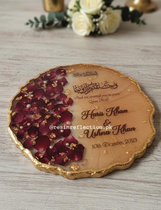 Personalized resin coaster with rose petals and engraved names on a wooden surface.